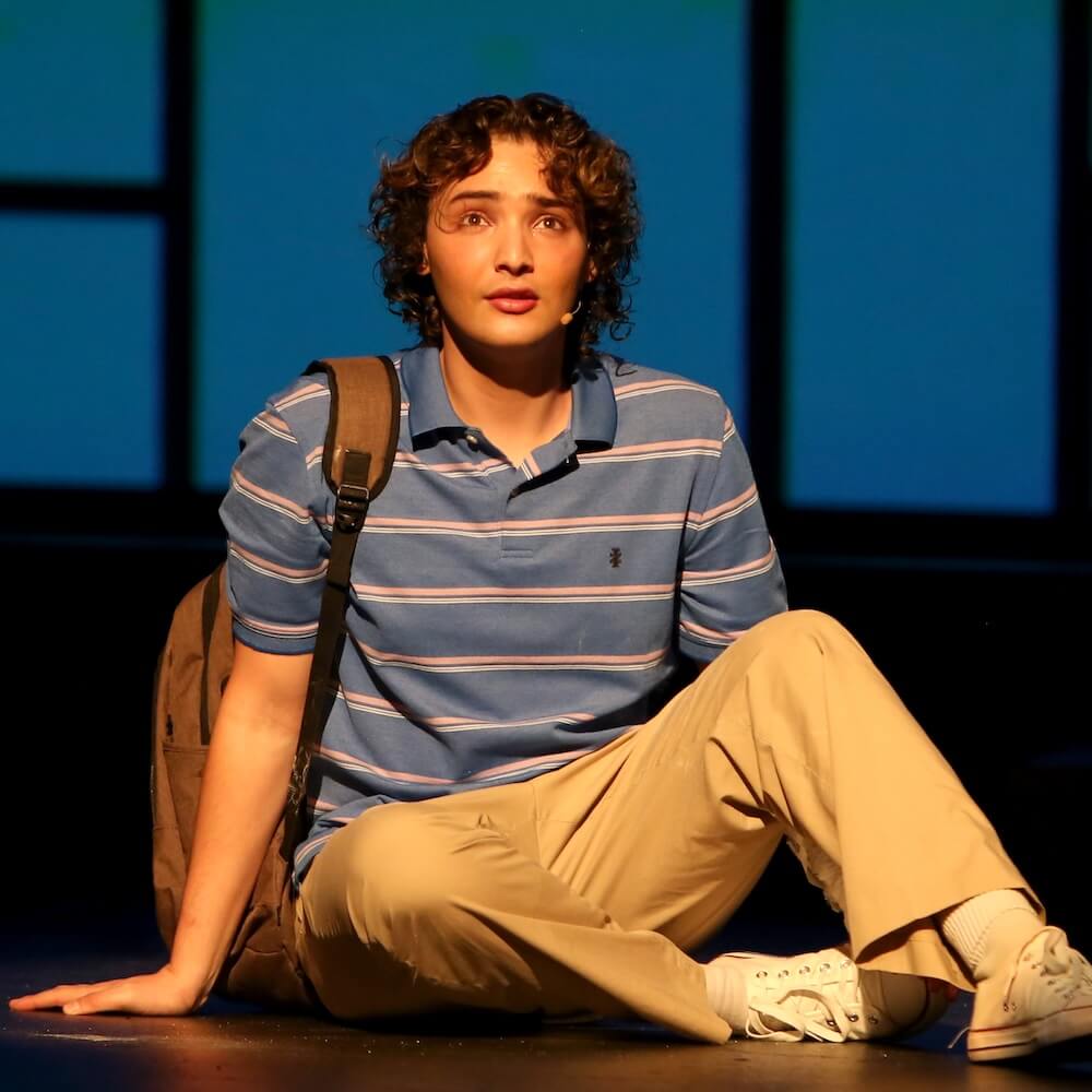 Actor Addison Brown as Evan Hansen sitting on stage looking regretful